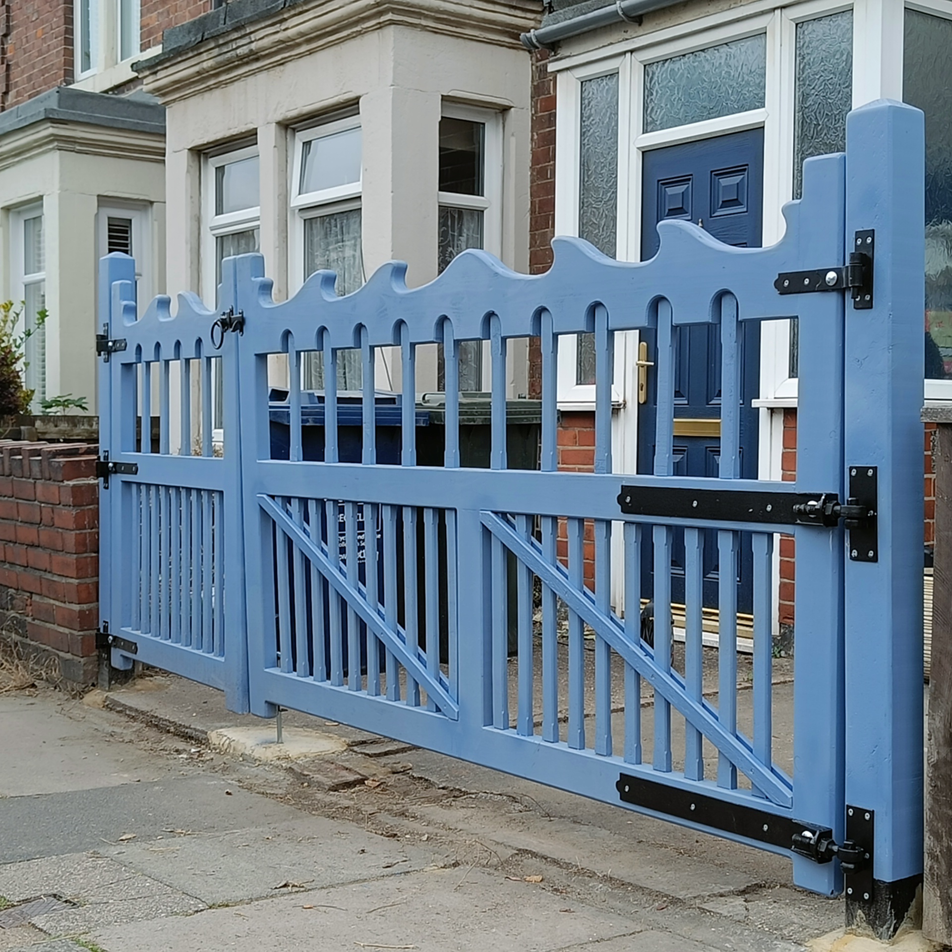 A set of two blue gates with a wave pattern on the top bar, picket infills with an arched detail.